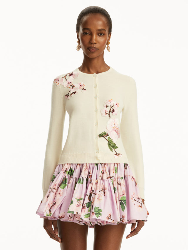 The model is wearing a white cardigan with pink cherry blossoms embroidered over a pink cherry blossom mini dress. Front View