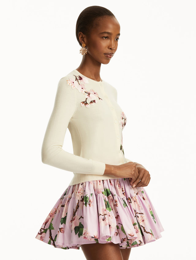 The model is wearing a white cardigan with pink cherry blossoms embroidered over a pink cherry blossom mini dress. Side View 