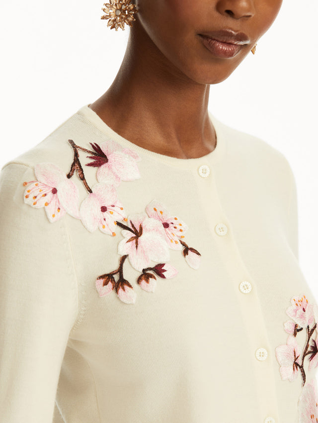 The model is wearing a white cardigan with pink cherry blossoms embroidered over a pink cherry blossom mini dress. Zoom View