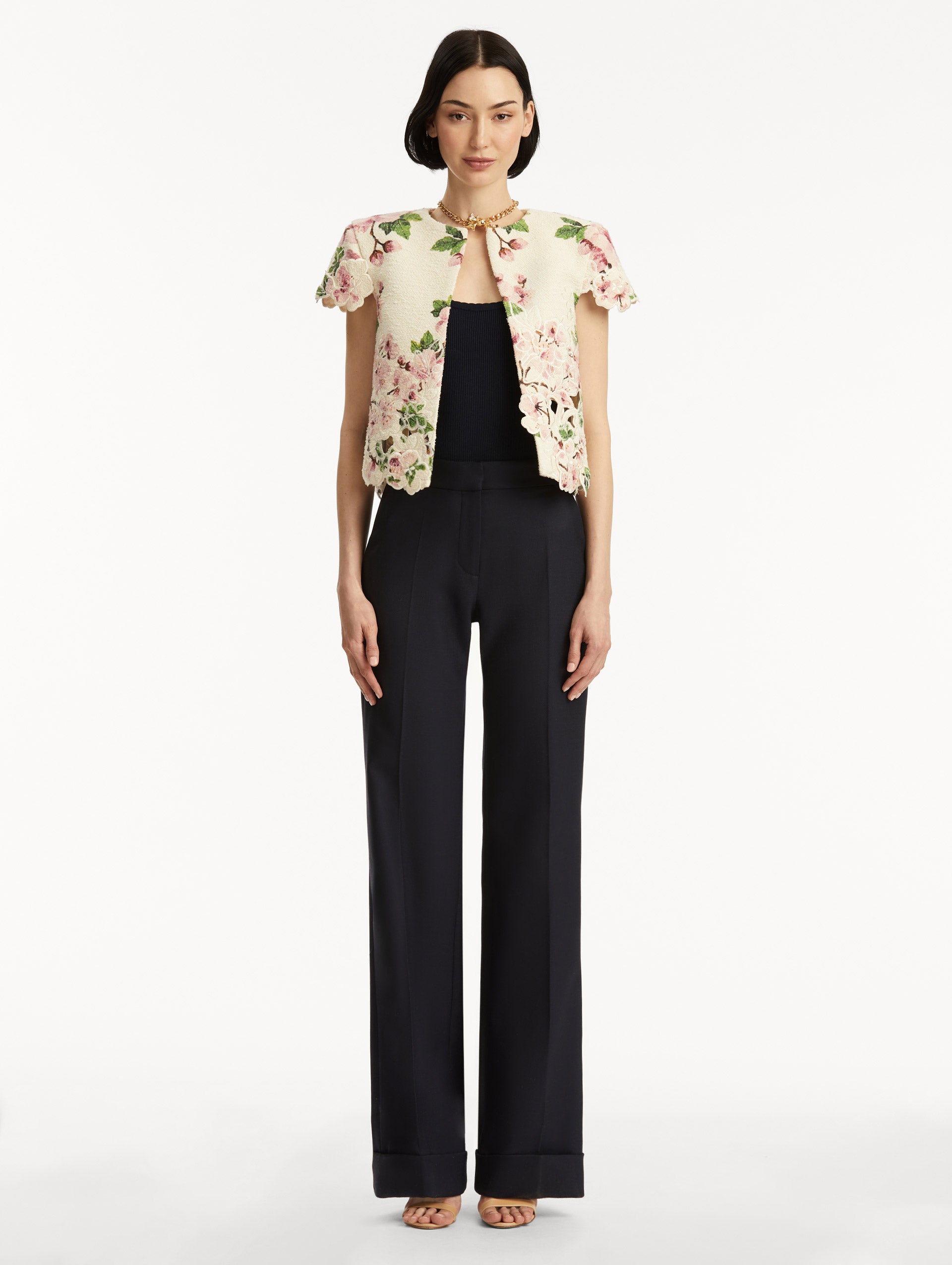 Model wearing white short sleeve tweed jacket with pink cherry blossoms embroidery. Paired with black pants and tank. Front view