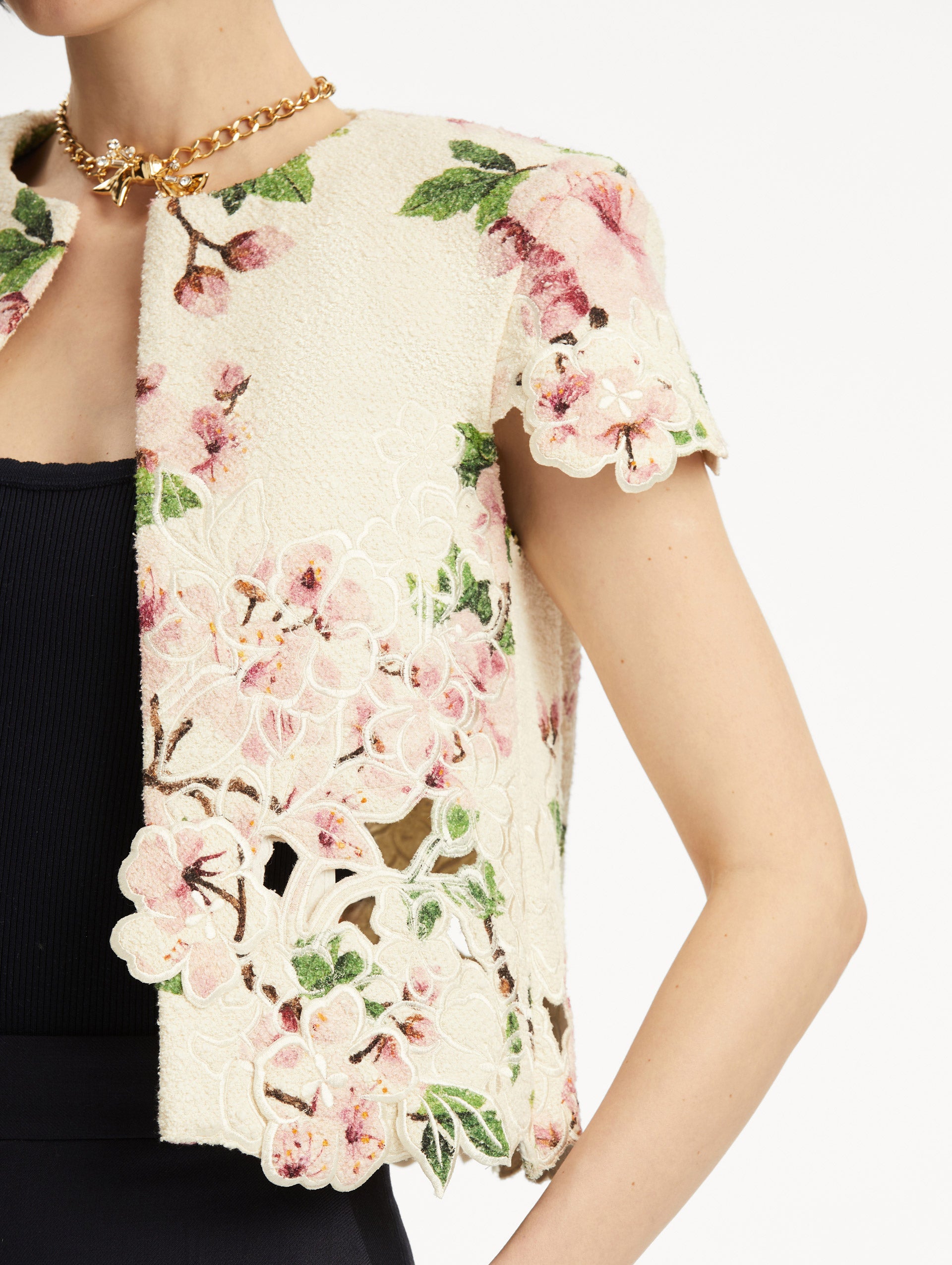 Model wearing white short sleeve tweed jacket with pink cherry blossoms embroidery. Paired with black pants and tank. Zoom view