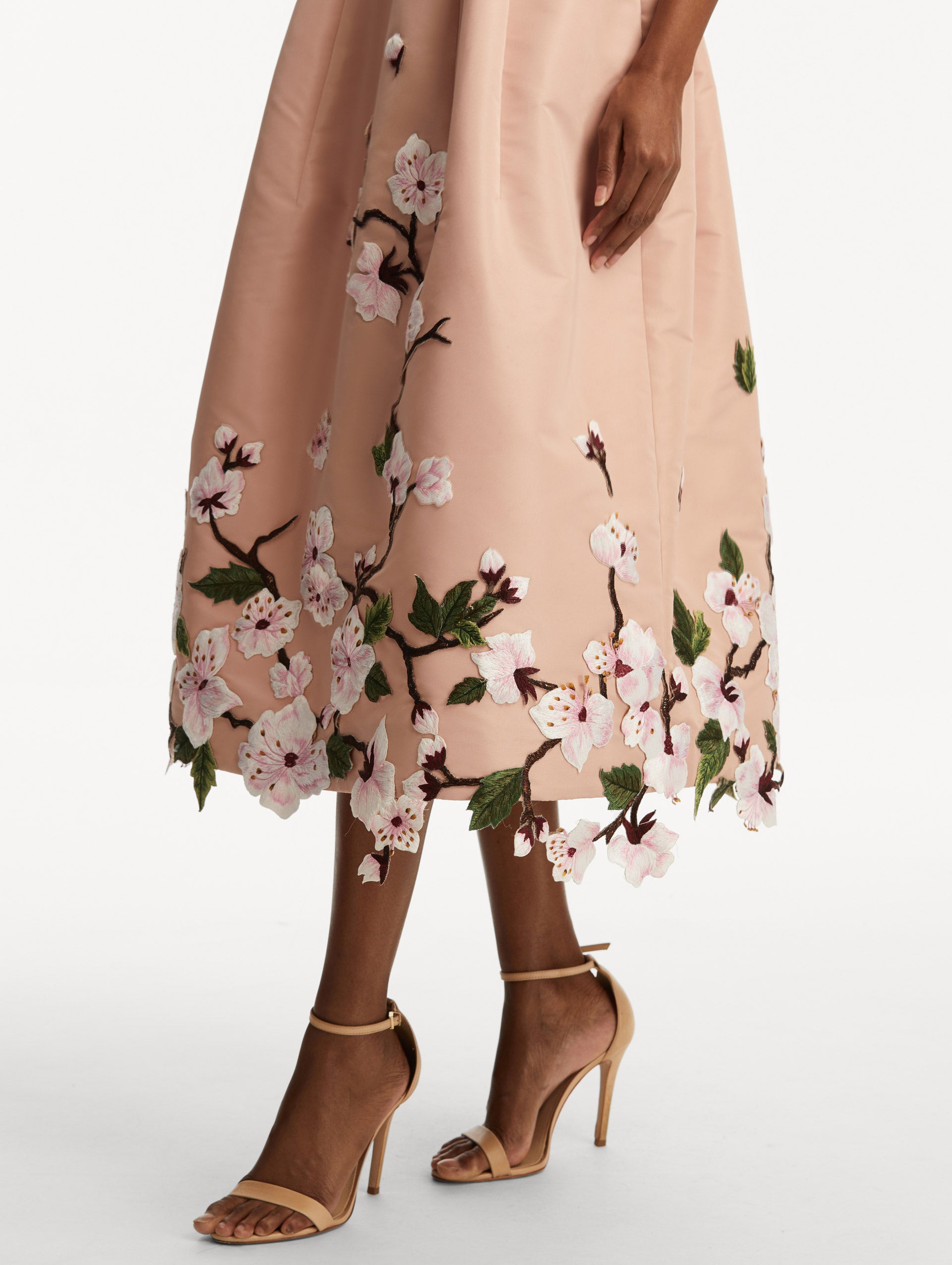Model wearing a blush pink sleeveless dress with cherry blossoms embroidered throughout the top and bottom. Zoom view