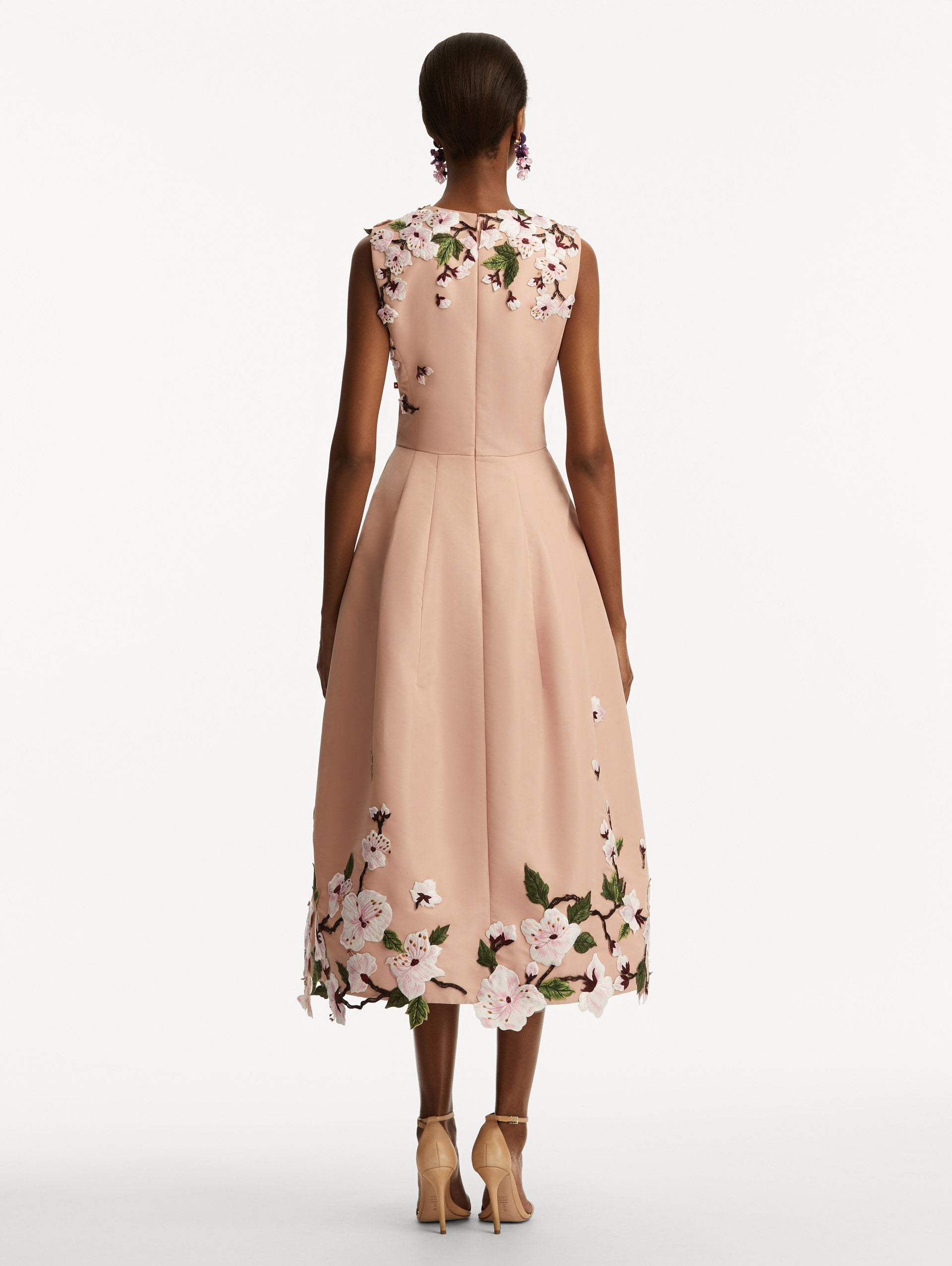 Model wearing a blush pink sleeveless dress with cherry blossoms embroidered throughout the top and bottom. Back view