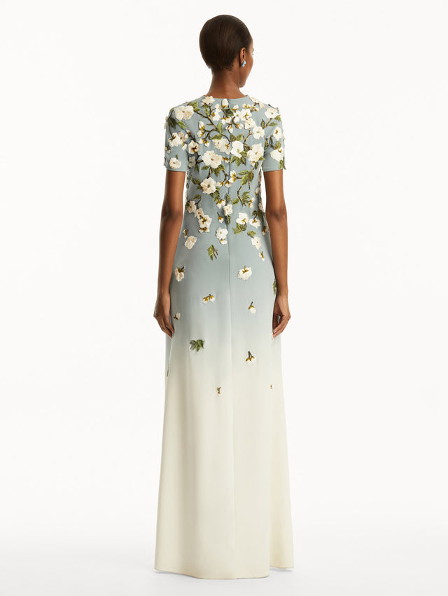 Model wearing Ombre light blue to white gown with short sleeves and white cherry blossoms embroidered. Back View