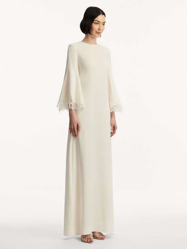 Model wearing white long sleeve caftan with lace detail on the cuff of the bell sleeves. Side view.