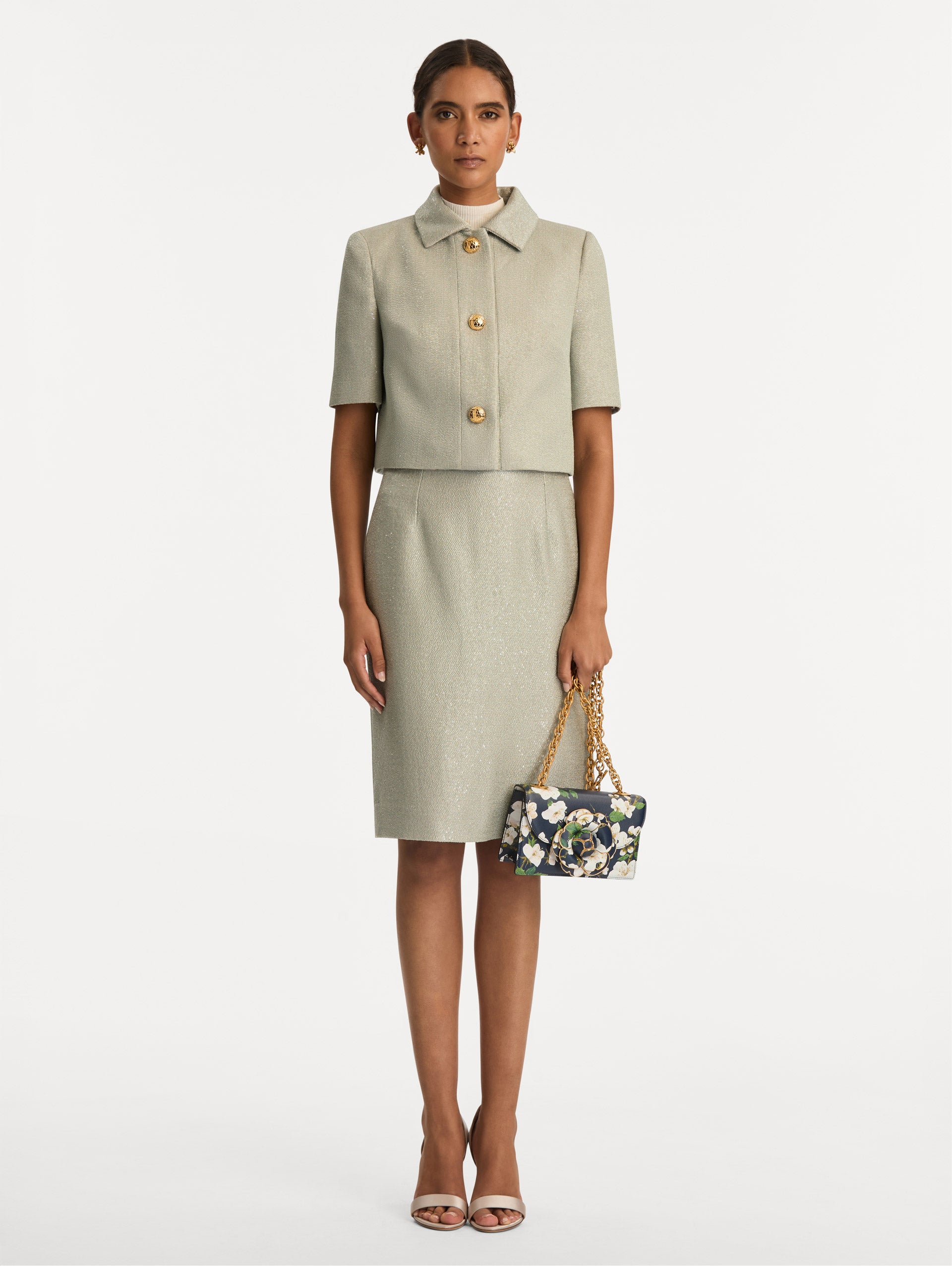 The TRO handbag in Navy with pink cherry blossoms all over. The bag has a three-dimensional flower at the center, and it has gold detailing in the border of each metal as well as a gold chain as strap. Front view.