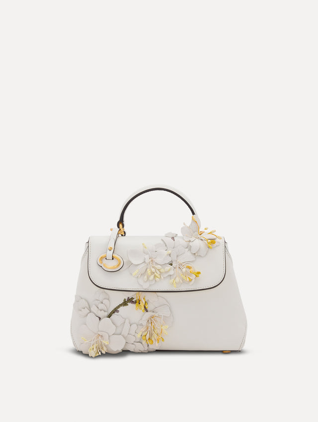 The Mini Poppy handbag in ivory with three-dimensional flowers attached. This bag comes with the Oscar O logo around the top handle, and a detachable shoulder strap. Front View.