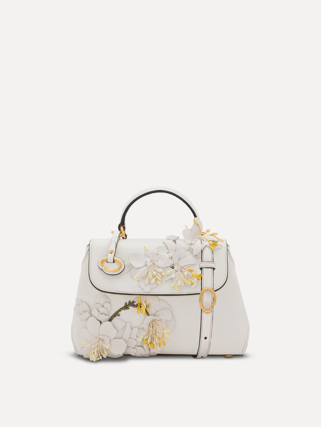 The Mini Poppy handbag in ivory with three-dimensional flowers attached. This bag comes with the Oscar O logo around the top handle, and a detachable shoulder strap. Front View.