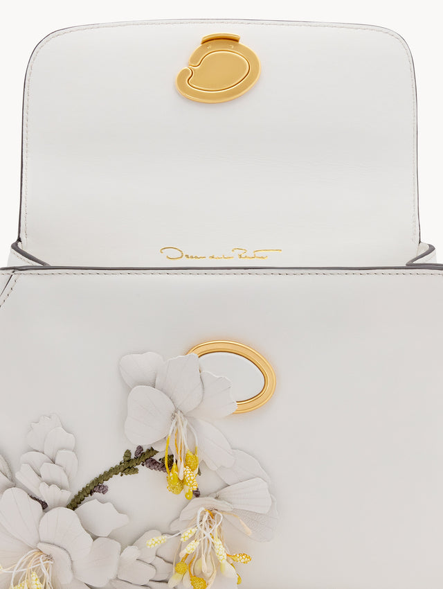 The Mini Poppy handbag in ivory with three-dimensional flowers attached. This bag comes with the Oscar O logo around the top handle, and a detachable shoulder strap. Zoom View.