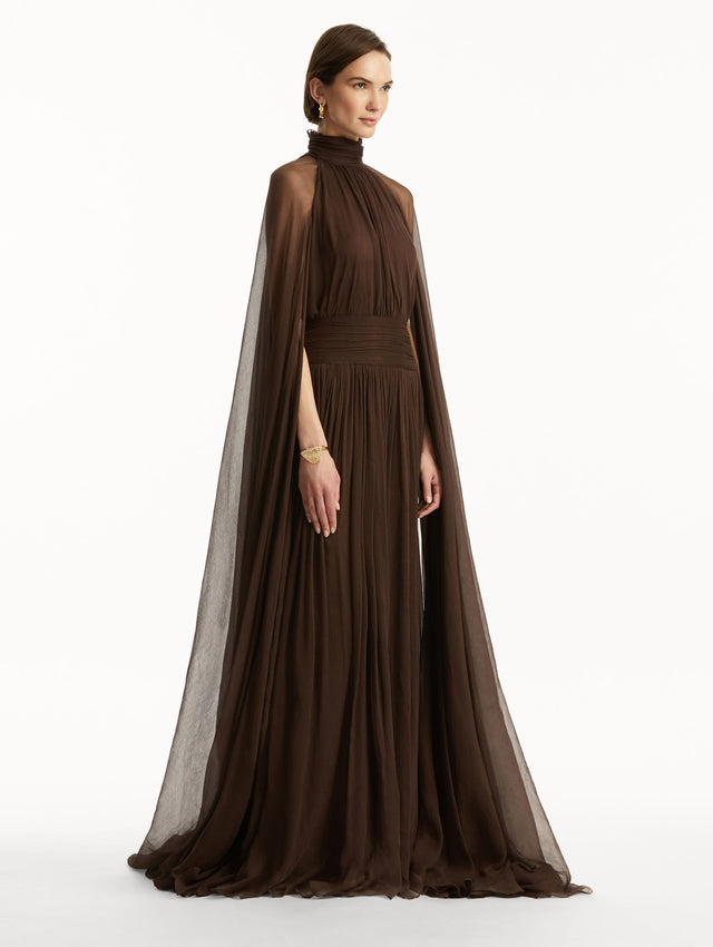 Brown chiffon gown with halter neck and long cascading sheer sleeves down the floor. Side view