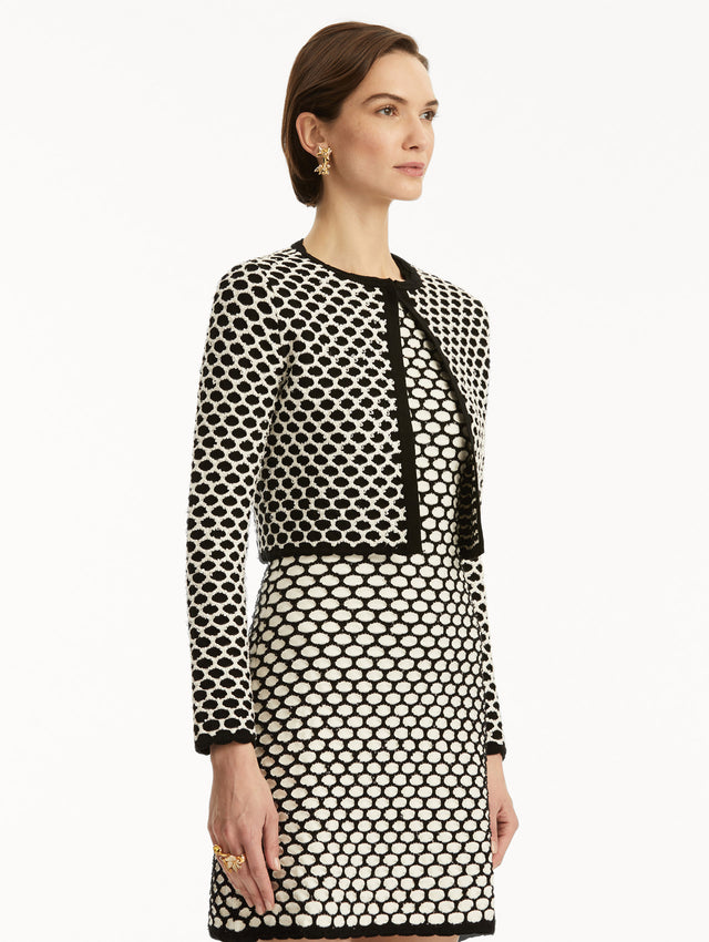 Model wearing black and white honeycomb print sequin knit jacket, paired with a matching dress. Side view