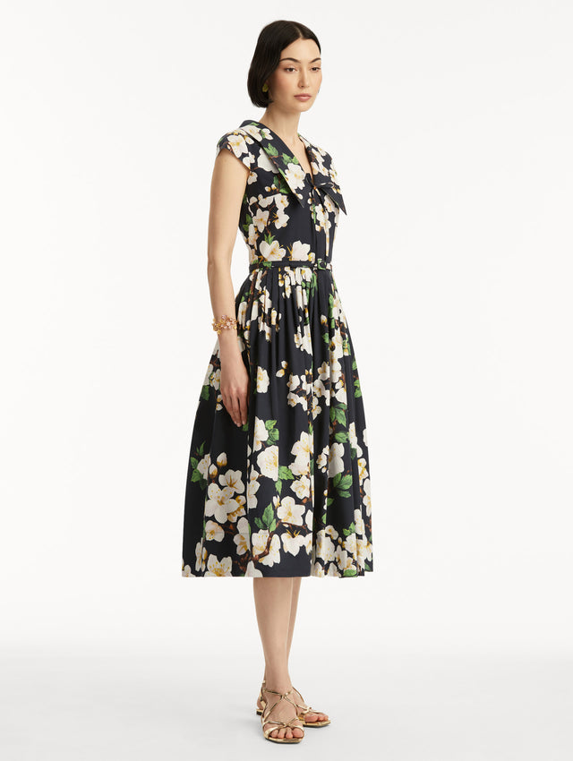 Model wears the Cherry Blossom Cotton Poplin Pleated Dress in a White and Navy floral print. Side View.