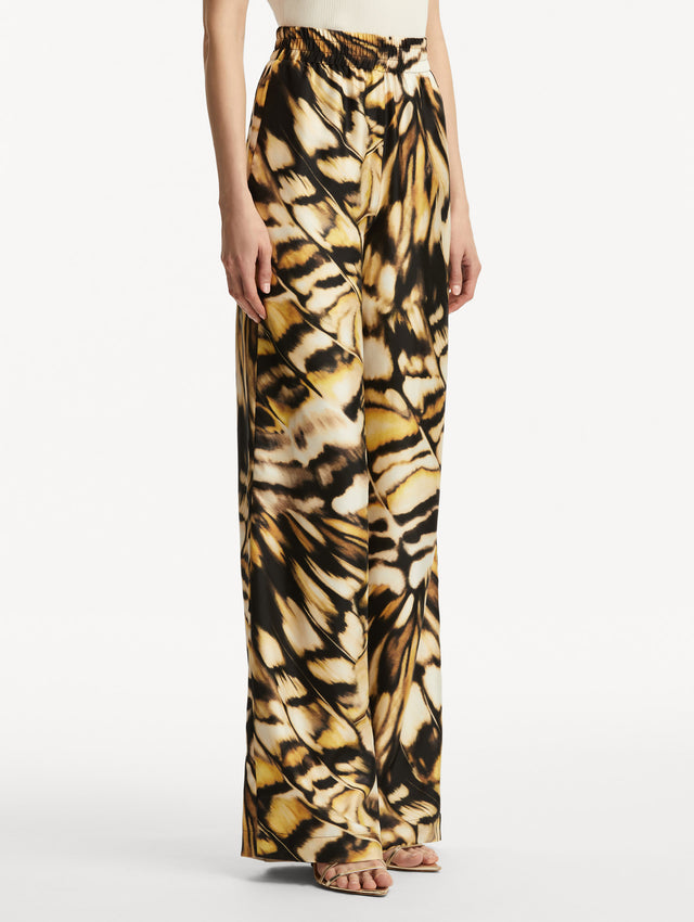 Abstract butterfly print in tones of yellow, brown/black, and white silk pants. Side view