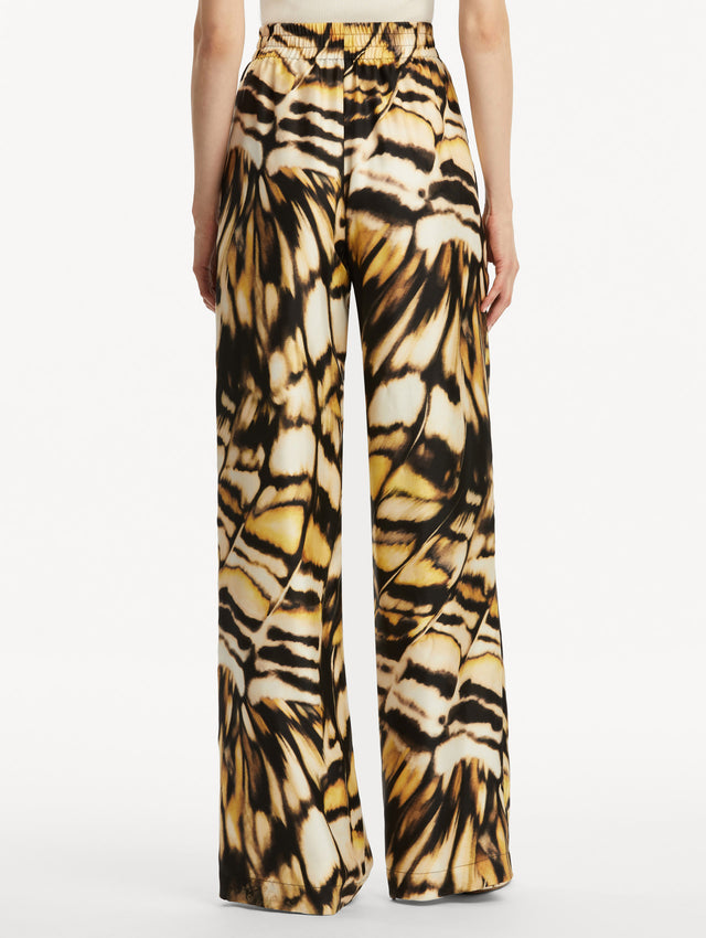 Abstract butterfly print in tones of yellow, brown/black, and white silk pants. Back view