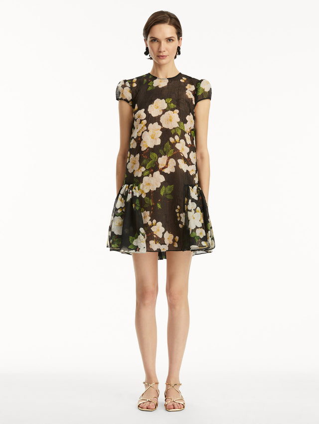 The model is wearing a short sleeve mini drop-waist dress in sheer black with white cherry blossoms printed all over. Front view.