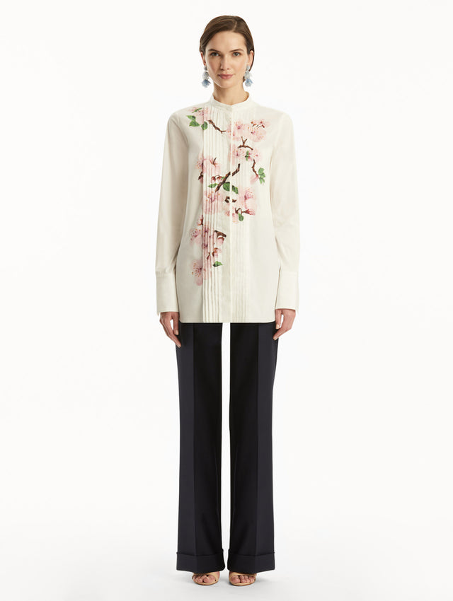 The model is wearing a white button-down blouse with pink cherry blossoms printed in the center. It is paired with Navy pants. Front view.