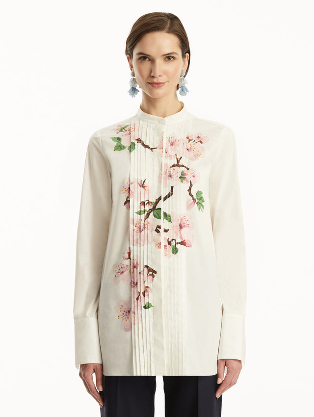 The model is wearing a white button-down blouse with pink cherry blossoms printed in the center. It is paired with Navy pants. Front view.