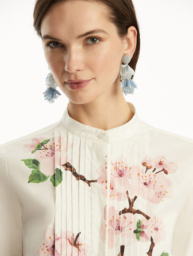 The model is wearing a white button-down blouse with pink cherry blossoms printed in the center. It is paired with Navy pants. Zoom view.