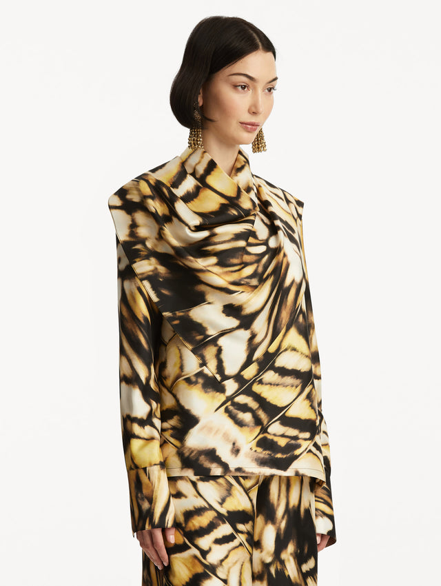 The model is wearing an abstract butterfly printed silk blouse, with draping around the neck, paired with matching pants. Side View. 