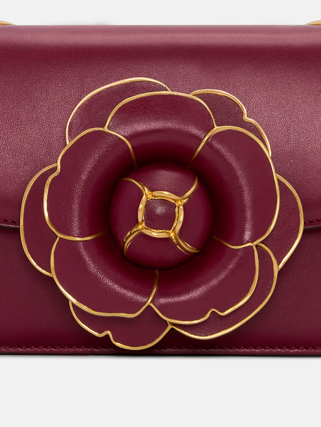 TRO Bag in red with flower applique at the clasp and gold detailing in the border of every petal. The bag also has a detachable gold shoulder strap. Zoom view