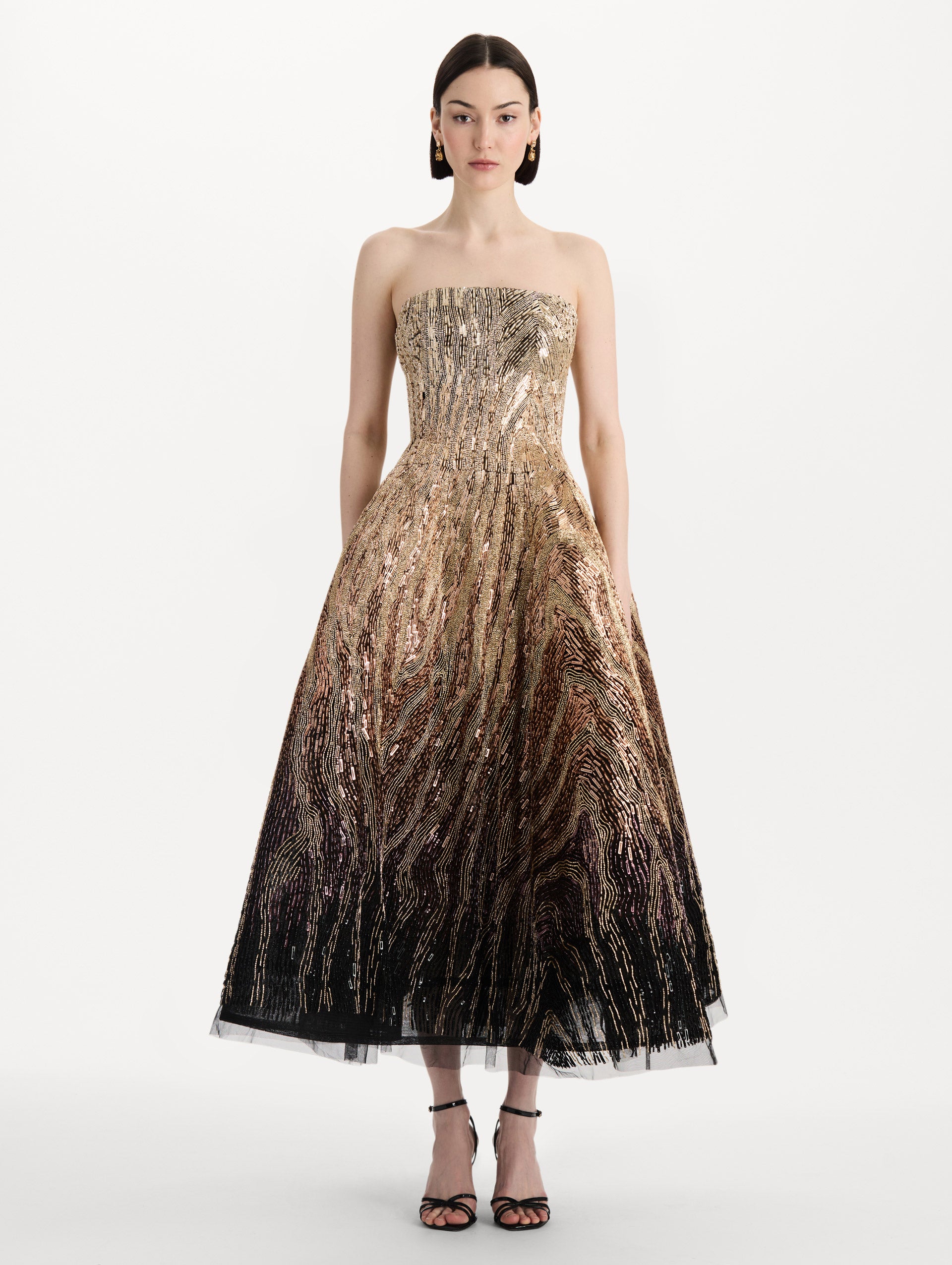 The model is wearing the beaded sequin moiré ombré tea length gown with a strapless silhouette and transitioning gold multi tones. Front view.