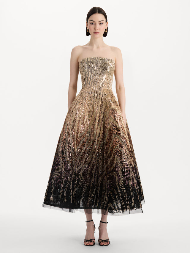 The model is wearing the beaded sequin moiré ombré tea length gown with a strapless silhouette and transitioning gold multi tones. Front view.