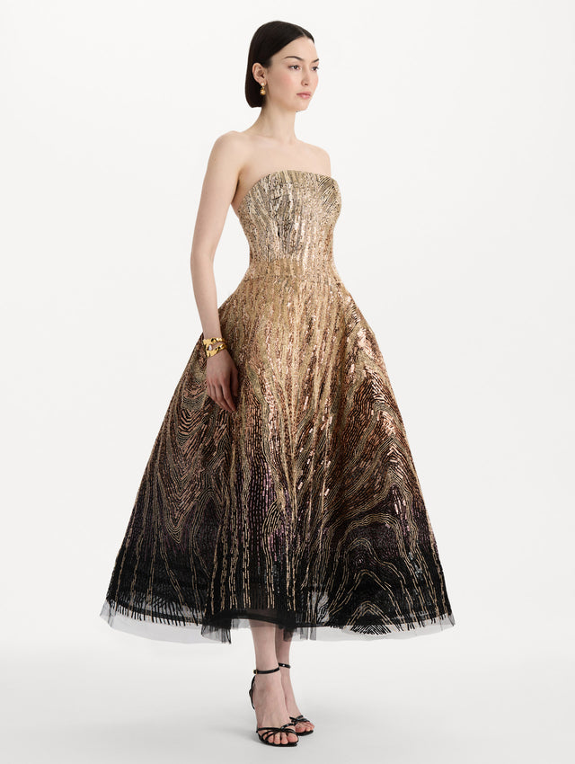 The model is wearing the beaded sequin moiré ombré tea length gown with a strapless silhouette and transitioning gold multi tones. Side view.