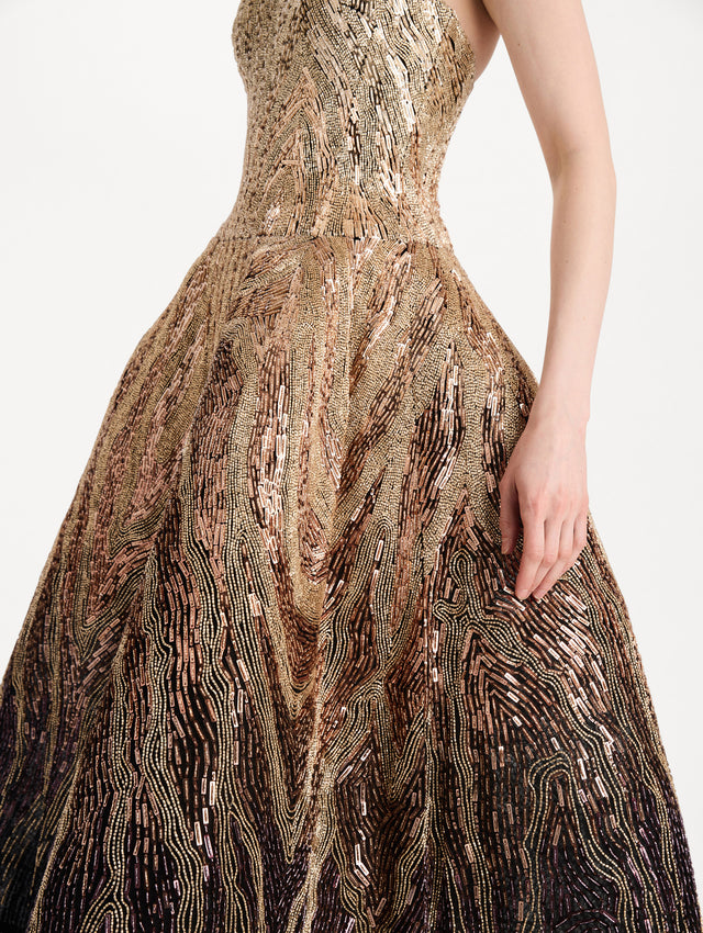 The model is wearing the beaded sequin moiré ombré tea length gown with a strapless silhouette and transitioning gold multi tones. Zoom view.