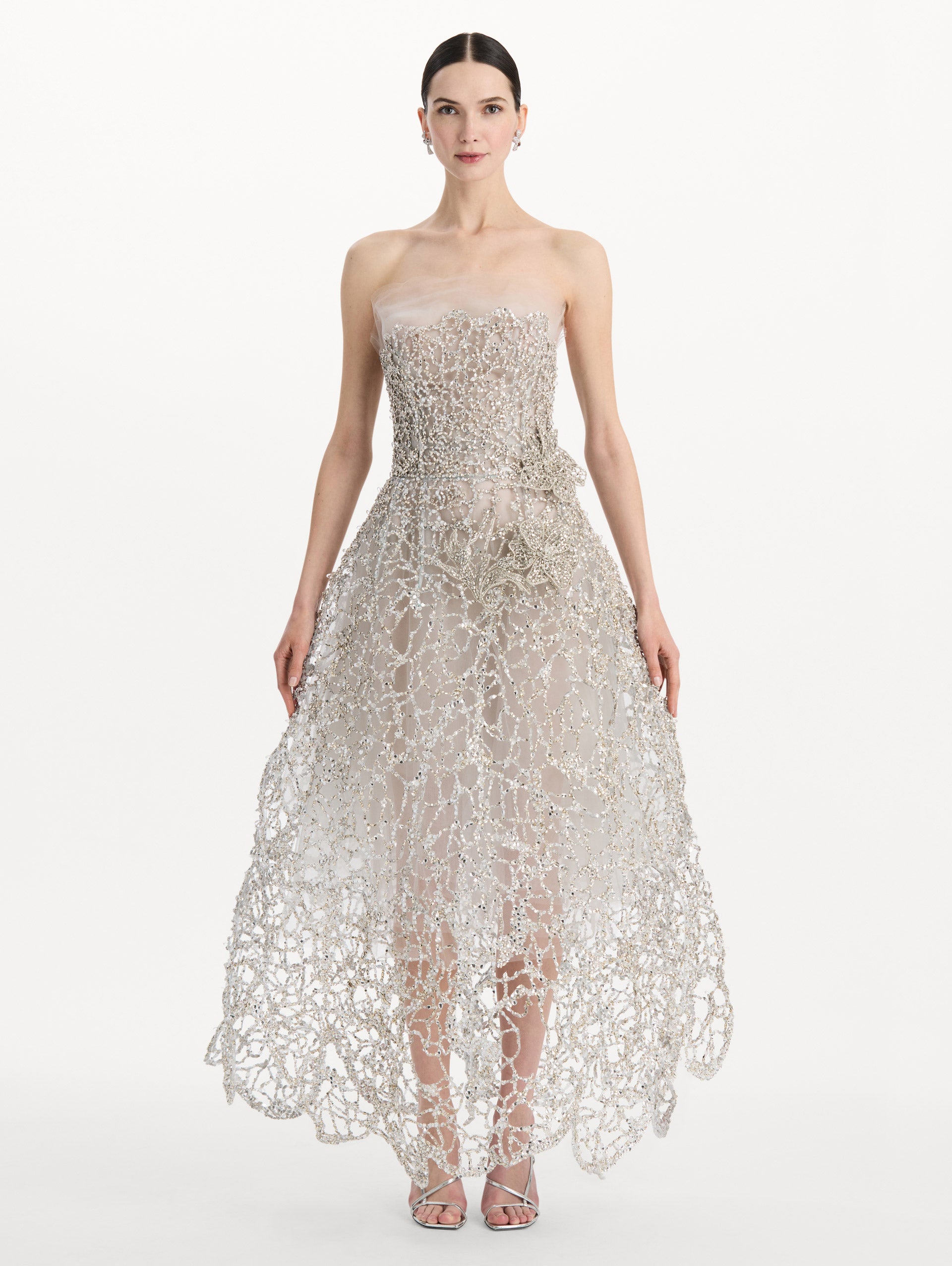 The model is wearing the crystal leaves embroidered gown with a strapless silhouette and crystal leaf detailing in the color silver. Front view.