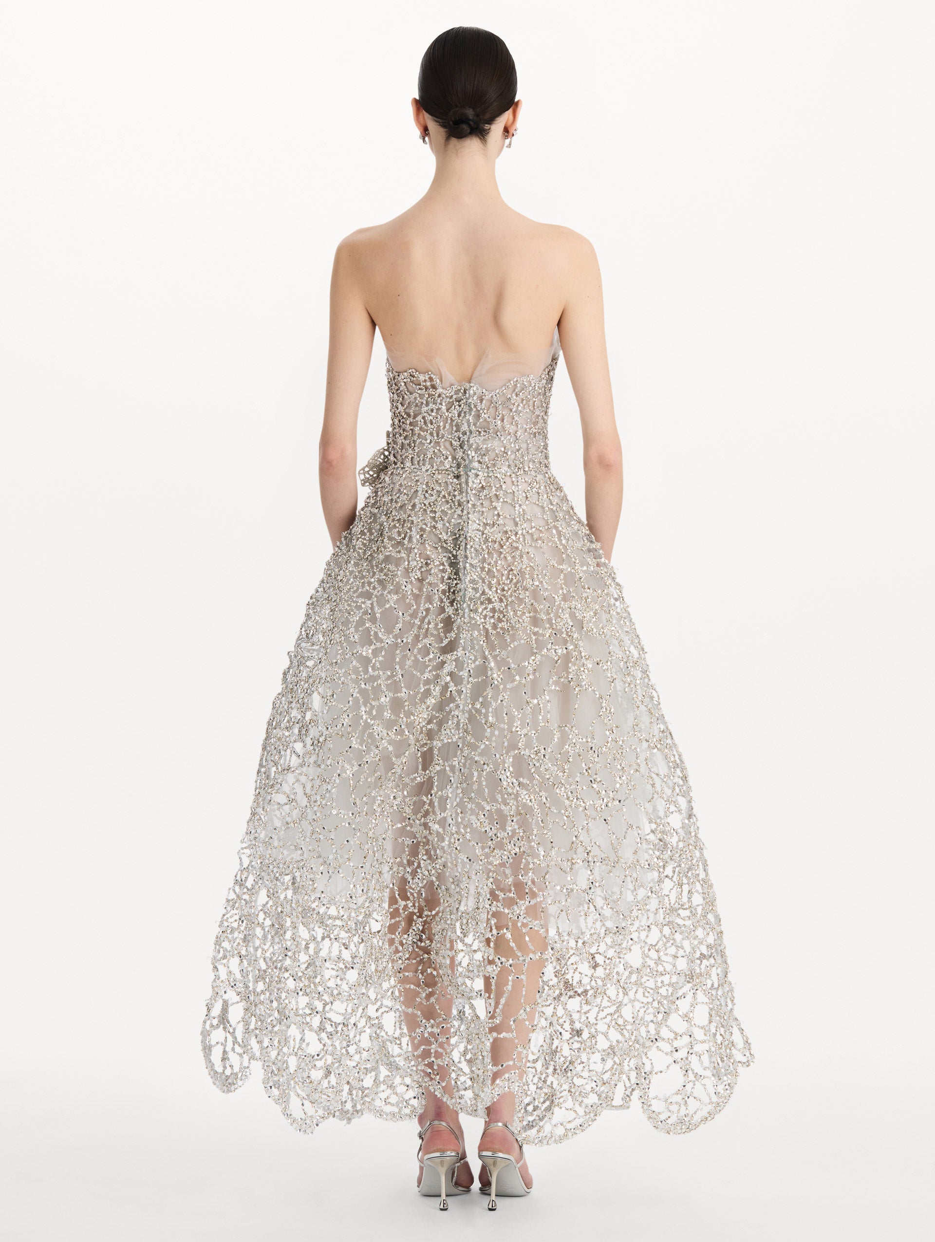 The model is wearing the crystal leaves embroidered gown with a strapless silhouette and crystal leaf detailing in the color silver. Back view.