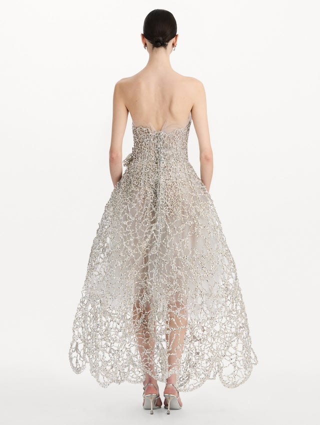 The model is wearing the crystal leaves embroidered gown with a strapless silhouette and crystal leaf detailing in the color silver. Back view.