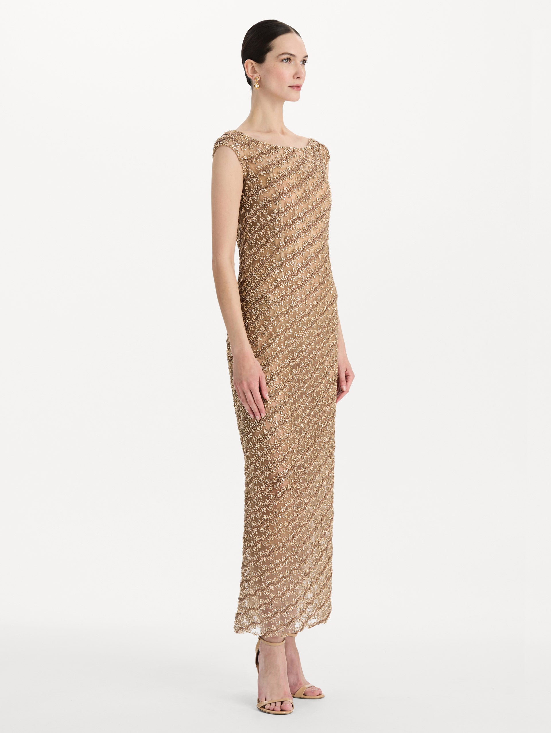 The model is wearing the beaded wave embroidered sleeveless cocktail dress in the color amber. Side view. 