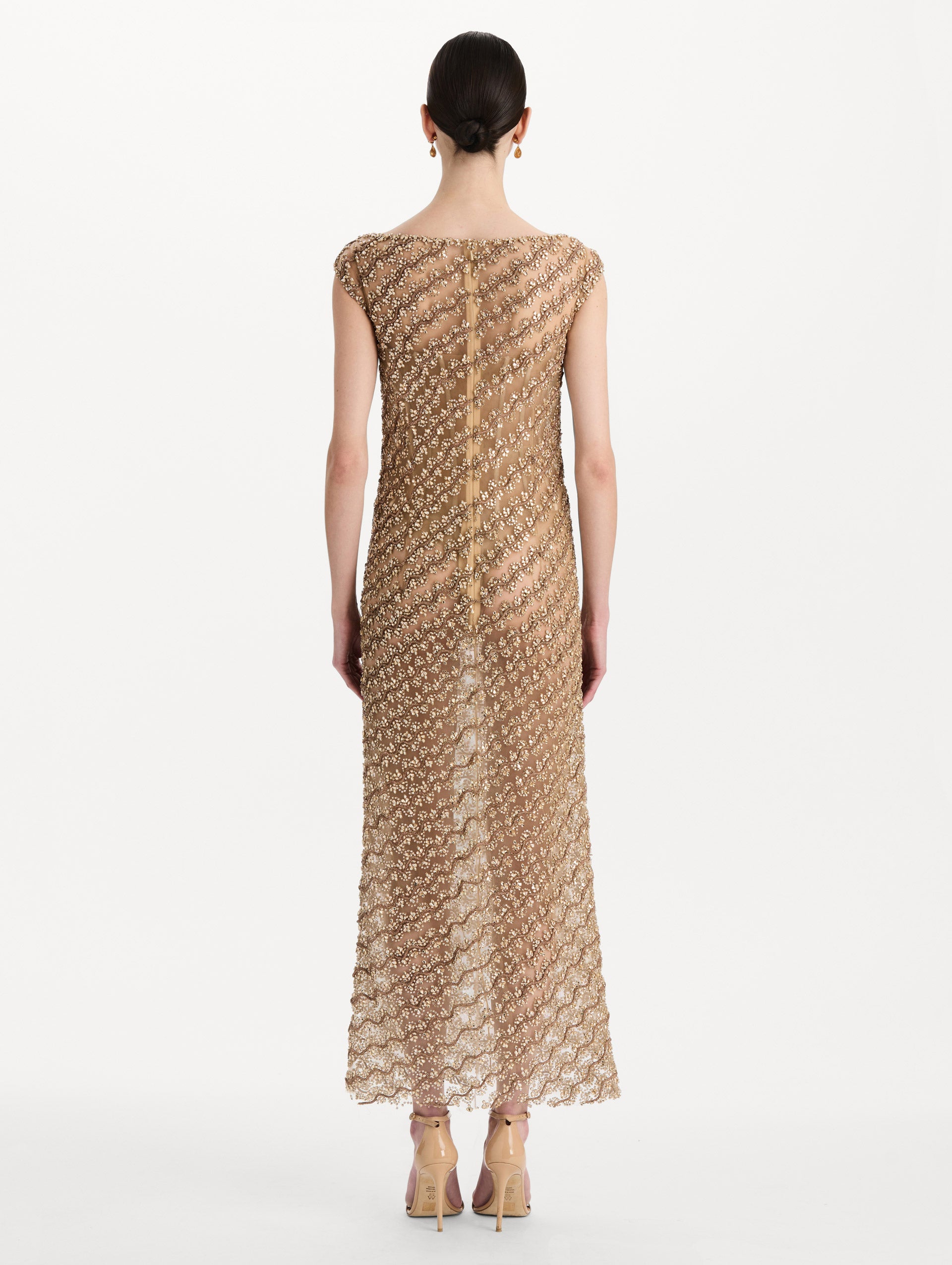 The model is wearing the beaded wave embroidered sleeveless cocktail dress in the color amber. Back view. 