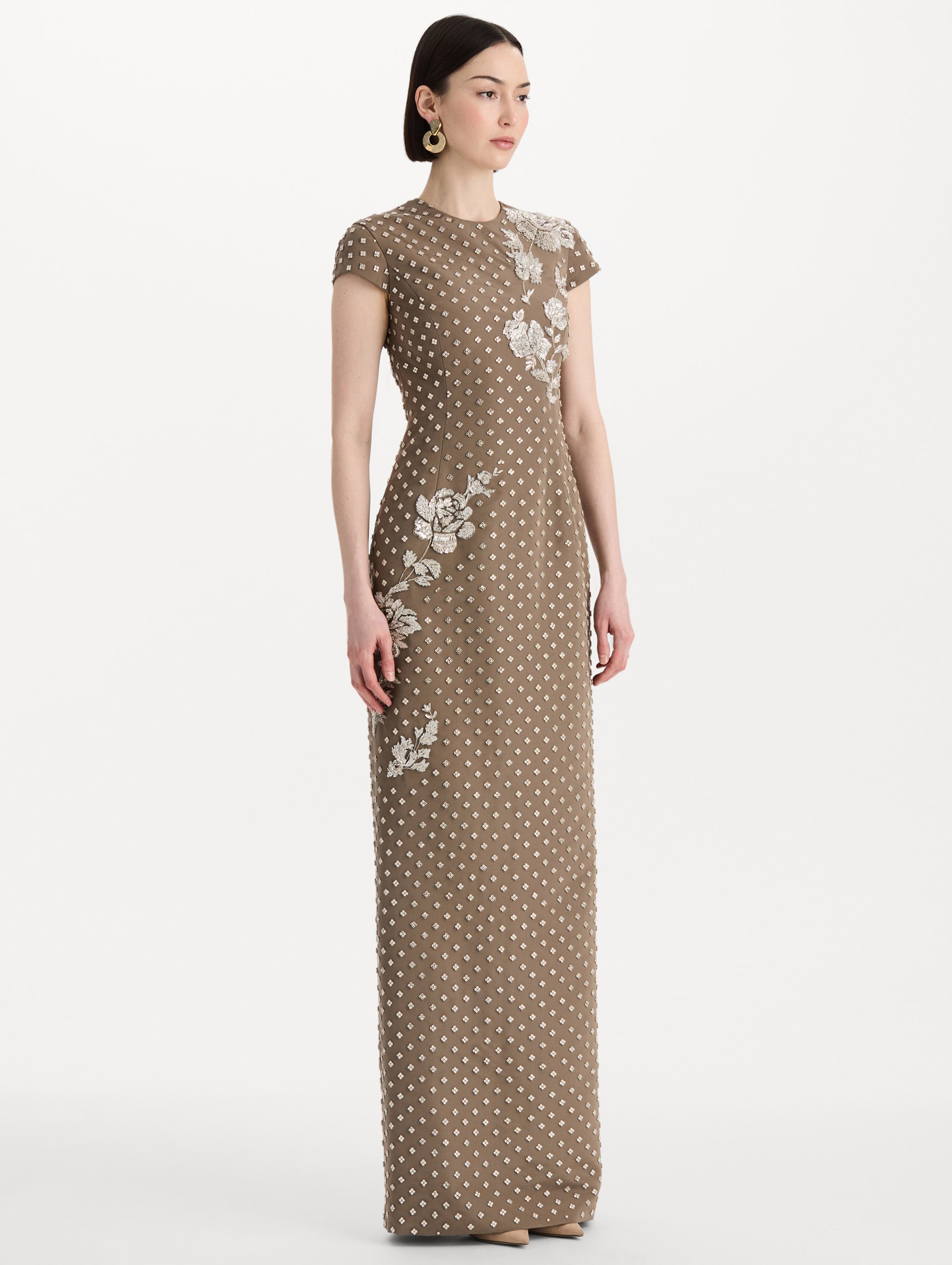 The model is wearing the crystal grid floral embroidered gown with short sleeves in the color stone. Side view. 