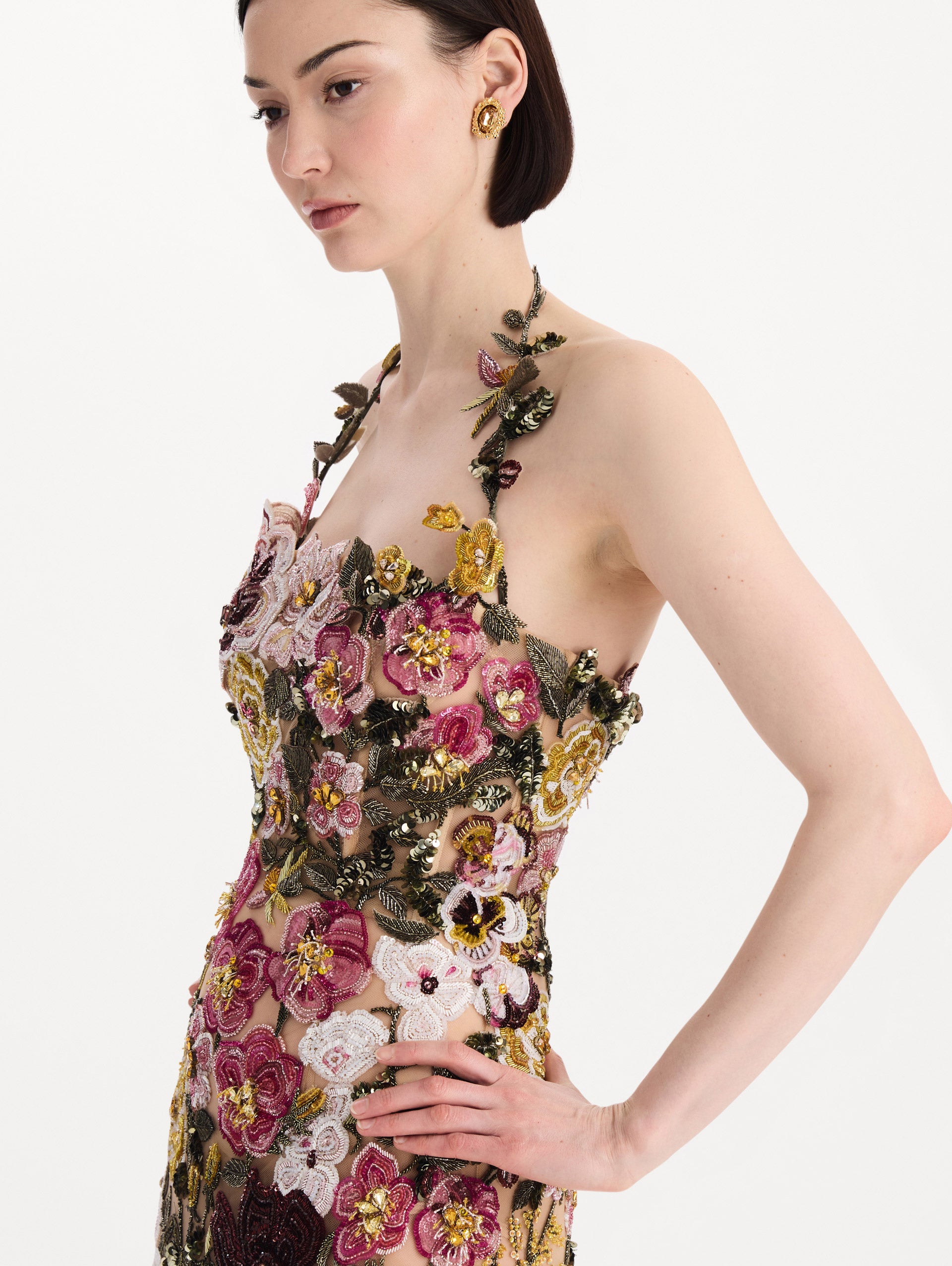 The model is wearing the beaded mixed botanical embroidered gown in multi-color with a halter neckline and floral detailing. Zoom view.