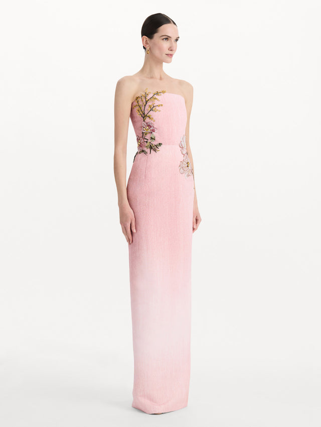 The model is wearing the beaded mixed botanical embroidered column gown with floral detailing and a strapless silhouette in the color blush. Side view.