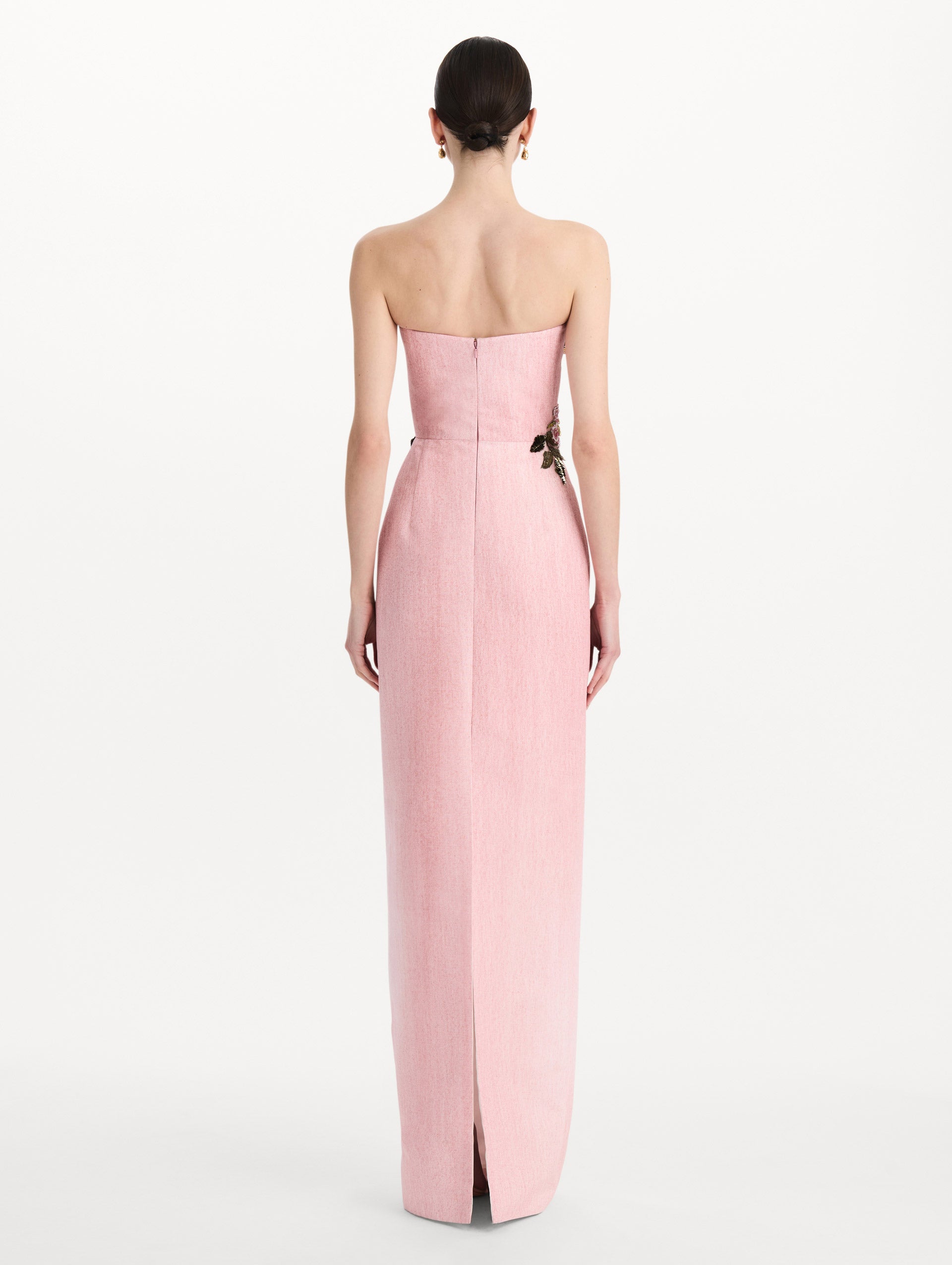 The model is wearing the beaded mixed botanical embroidered column gown with floral detailing and a strapless silhouette in the color blush. Back view.