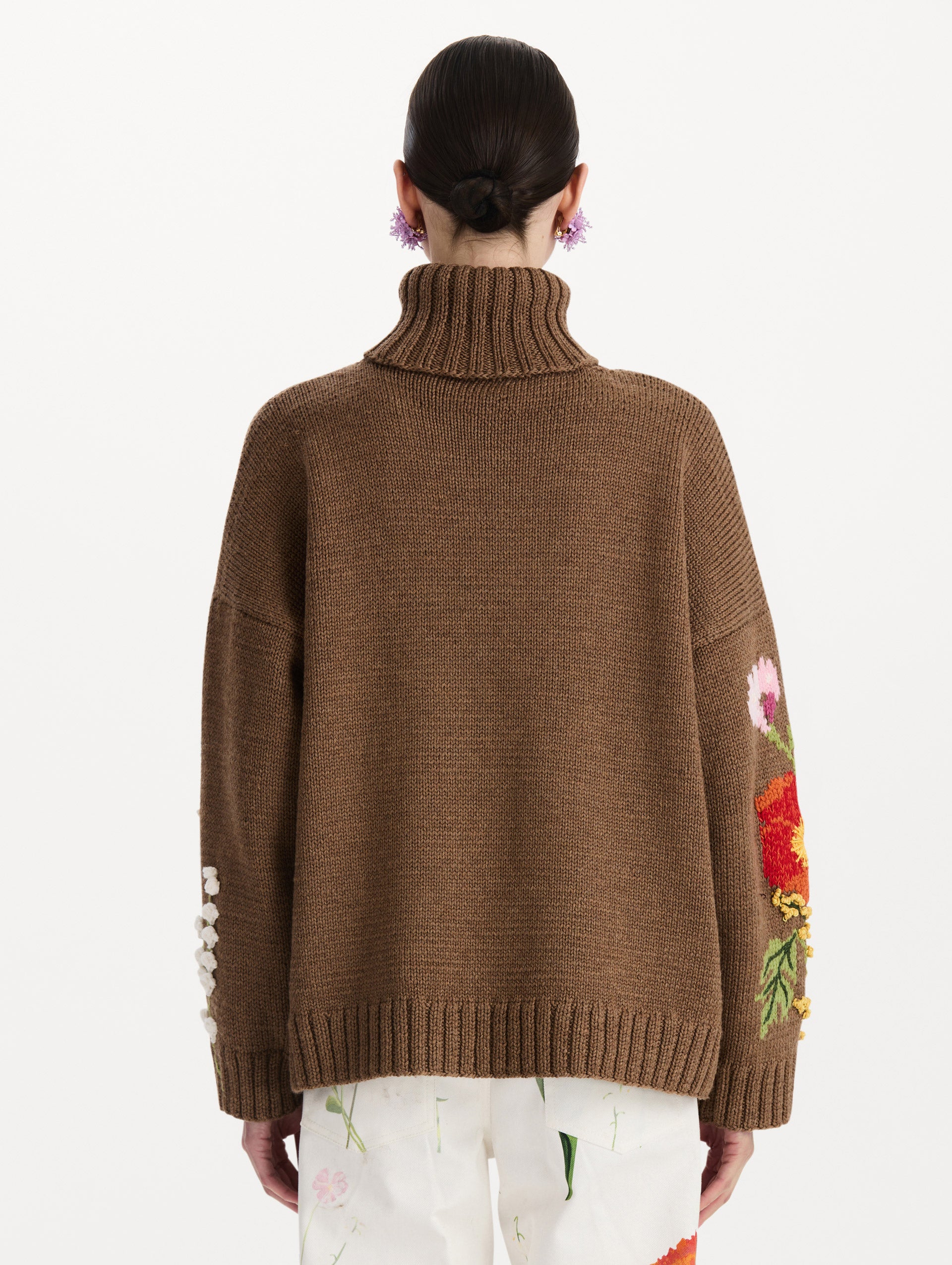 The model is wearing the mixed botanical embroidered oversized pullover with a floral intarsia pattern in the color brown. Back view. 