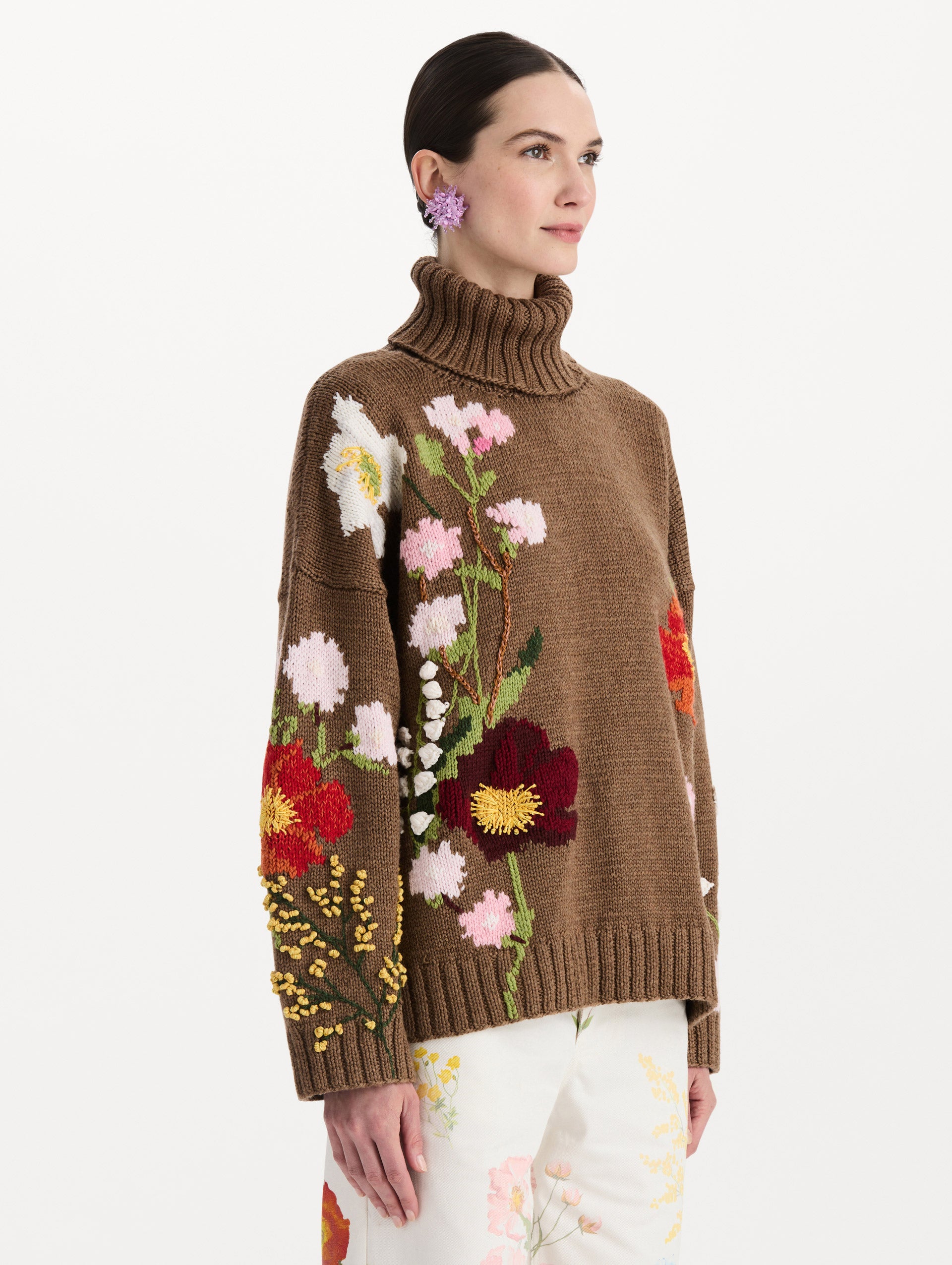 The model is wearing the mixed botanical embroidered oversized pullover with a floral intarsia pattern in the color brown. Side view. 
