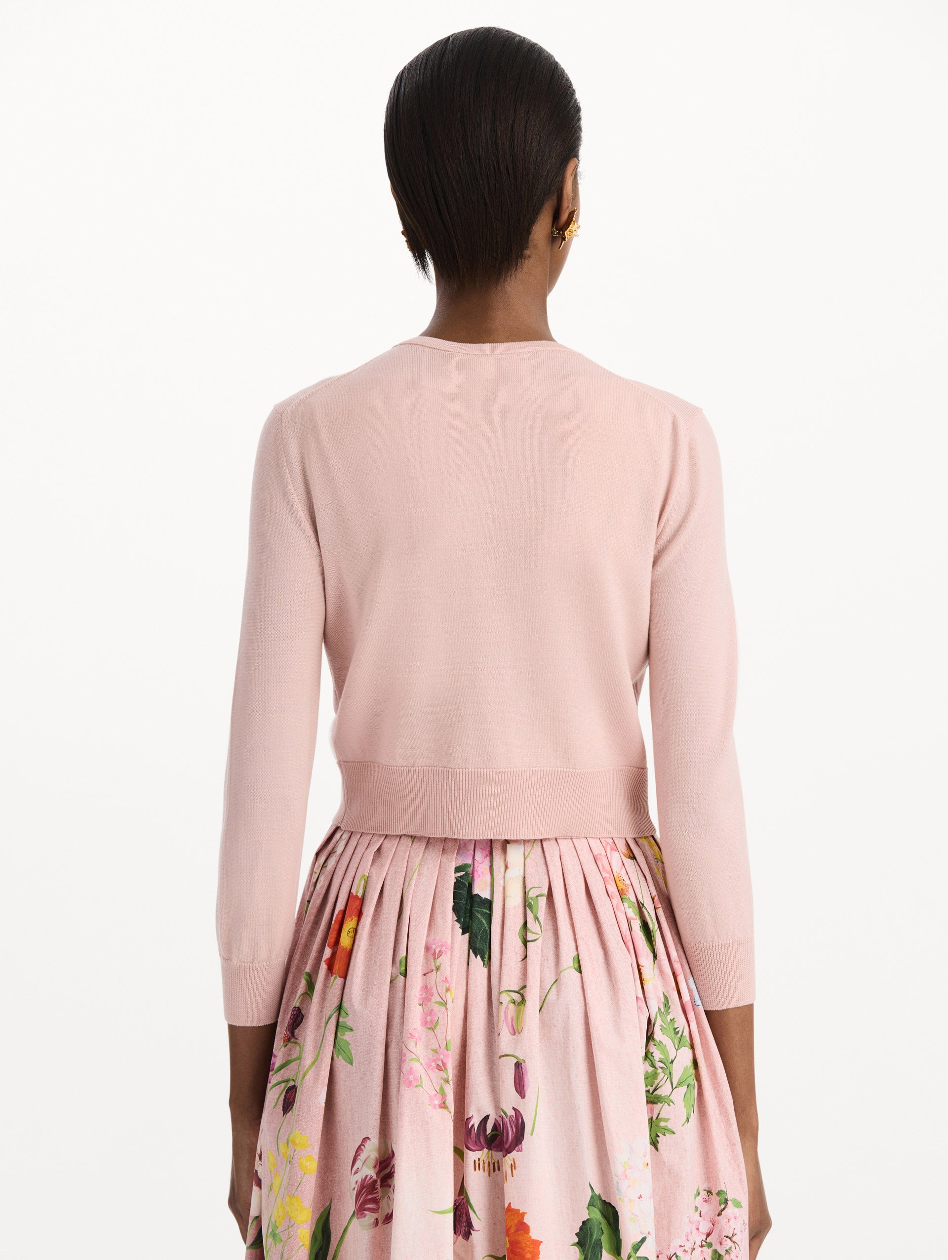 The model is wearing the mixed botanical threadwork cardigan in the color blush with floral detailing. Back view.