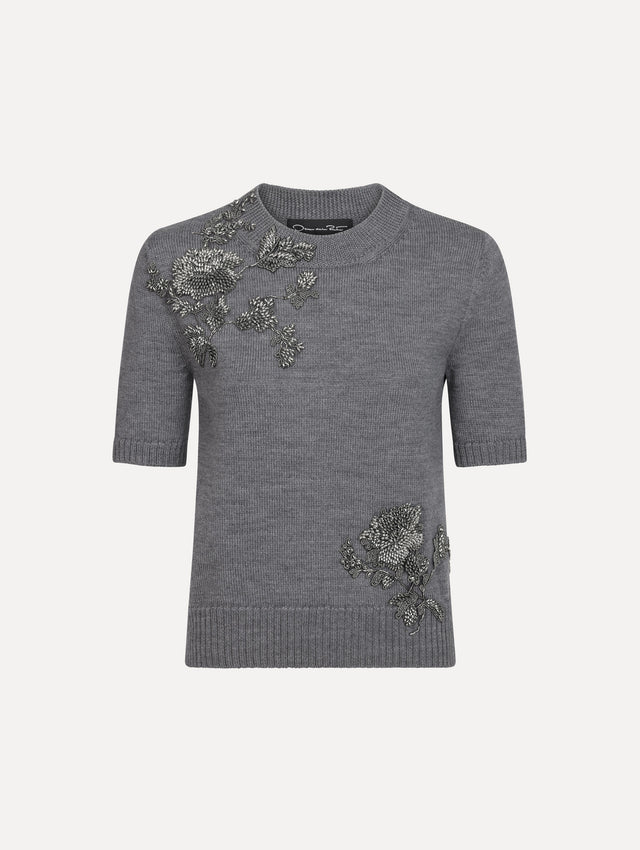 The model is wearing a beaded peony embroidered pullover in the color melange grey.