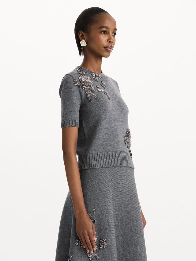 The model is wearing a beaded peony embroidered pullover in the color melange grey. Side view.