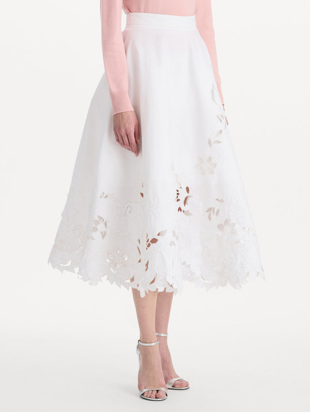 The model is wearing the floral cutout cotton twill skirt with botanical embroidery and a full silhouette in the color white. Side view.