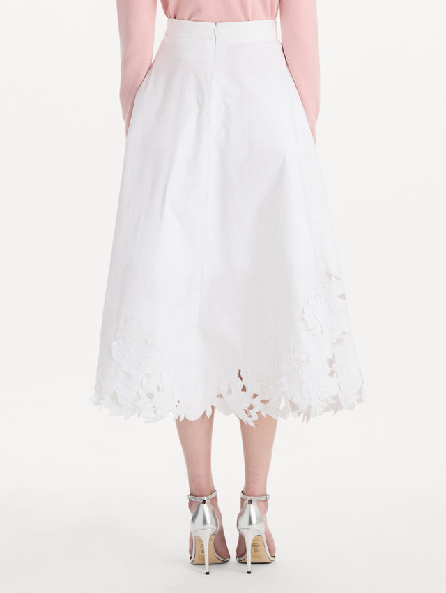 The model is wearing the floral cutout cotton twill skirt with botanical embroidery and a full silhouette in the color white. Back view.