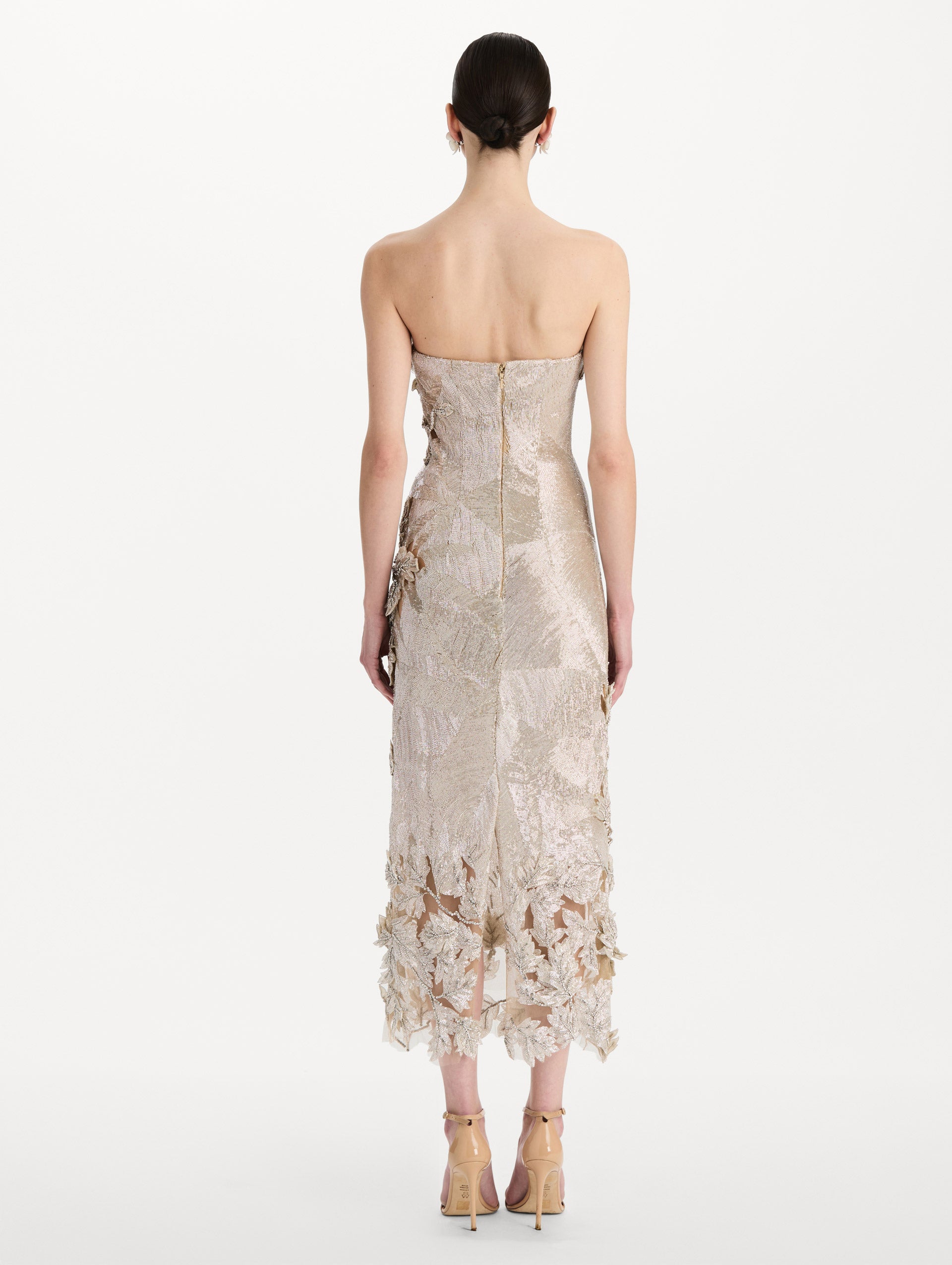 The model is wearing the intarsia leaves cutout embroidered cocktail dress with a strapless silhouette in the color silver. Back view.