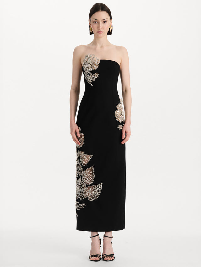 The model is wearing the crystal leaves embroidered cocktail dress with a strapless silhouette in the color black. Front view. 
