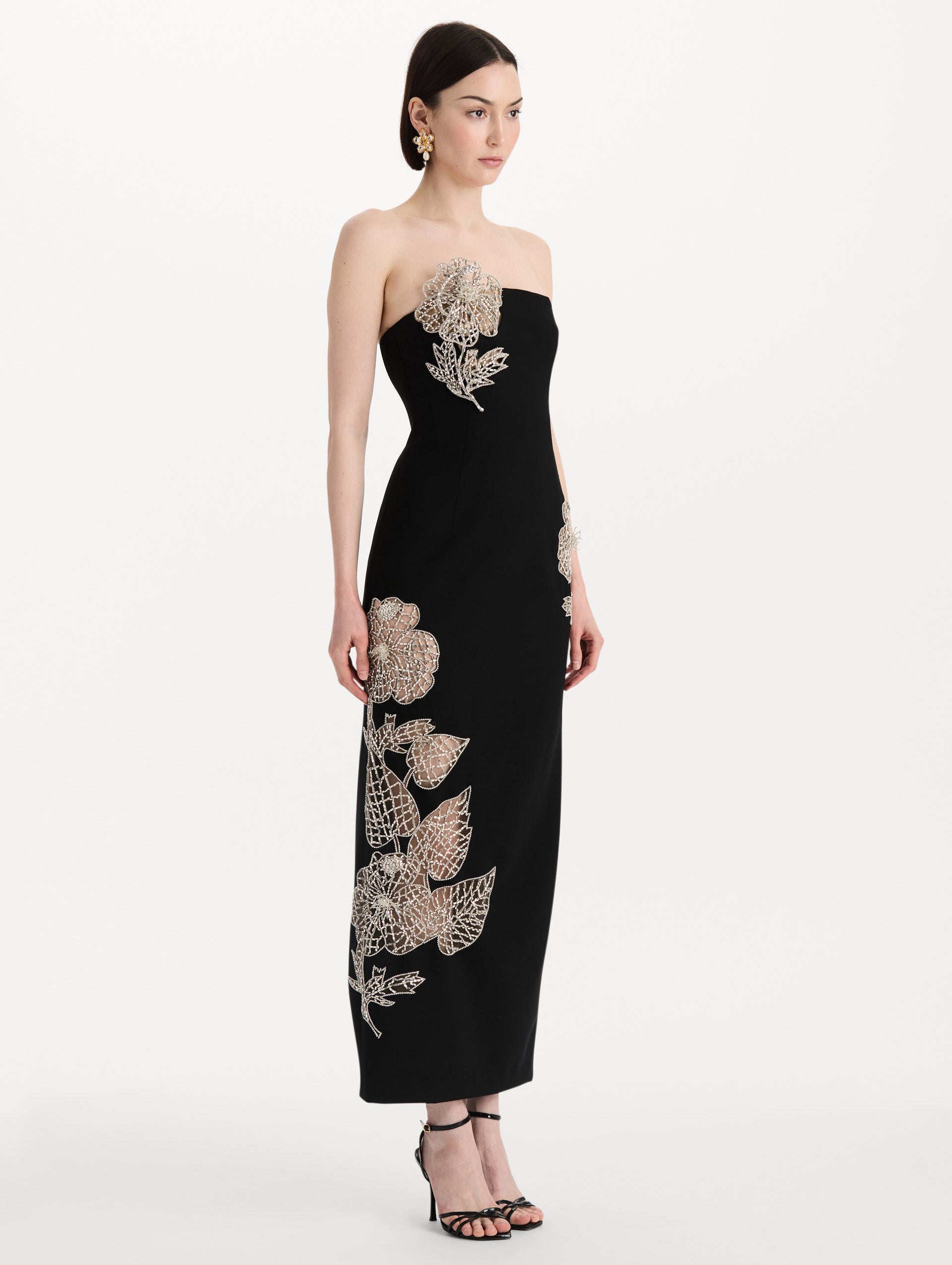 The model is wearing the crystal leaves embroidered cocktail dress with a strapless silhouette in the color black. Side view. 