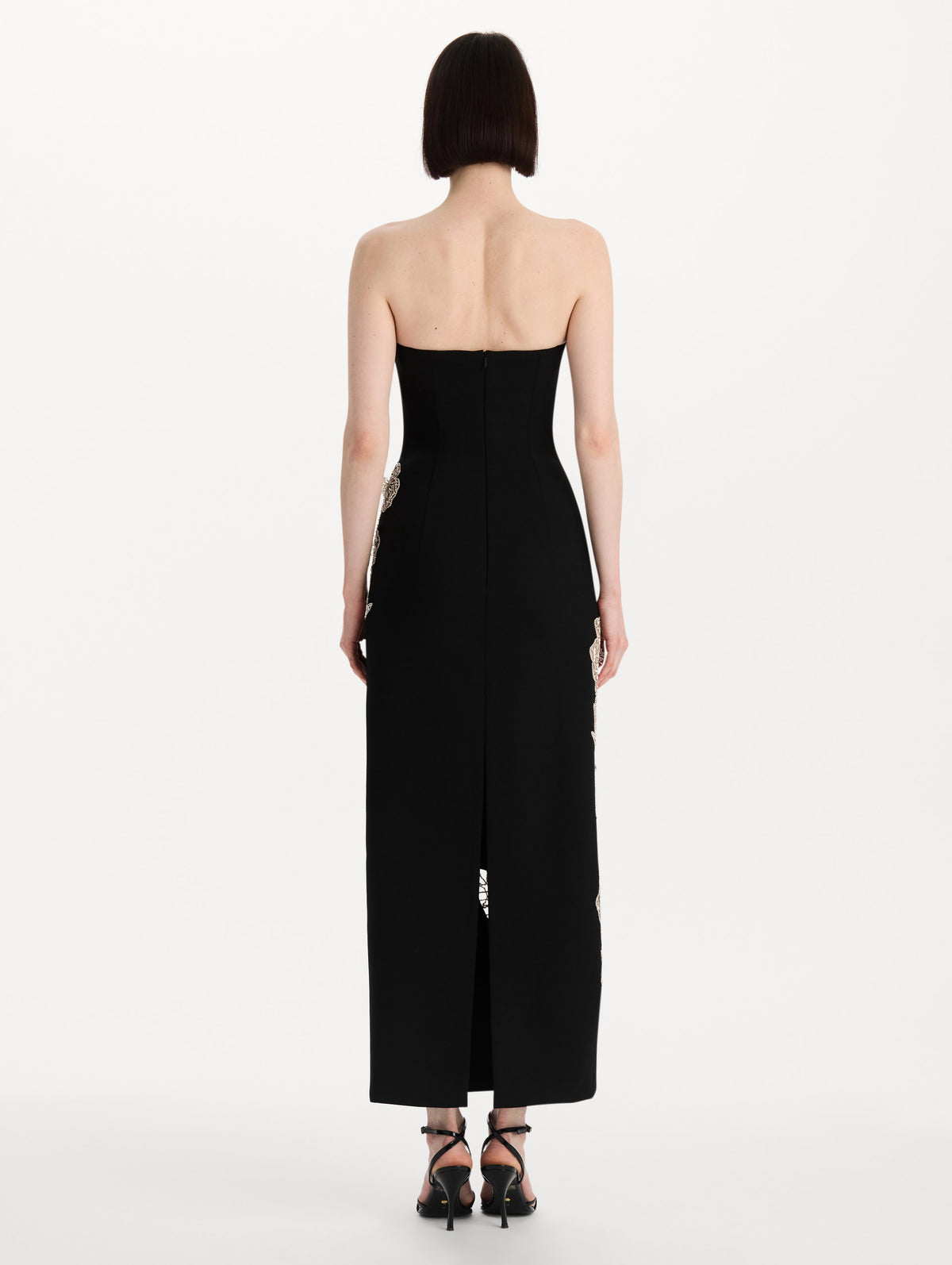 The model is wearing the crystal leaves embroidered cocktail dress with a strapless silhouette in the color black. Back view. 