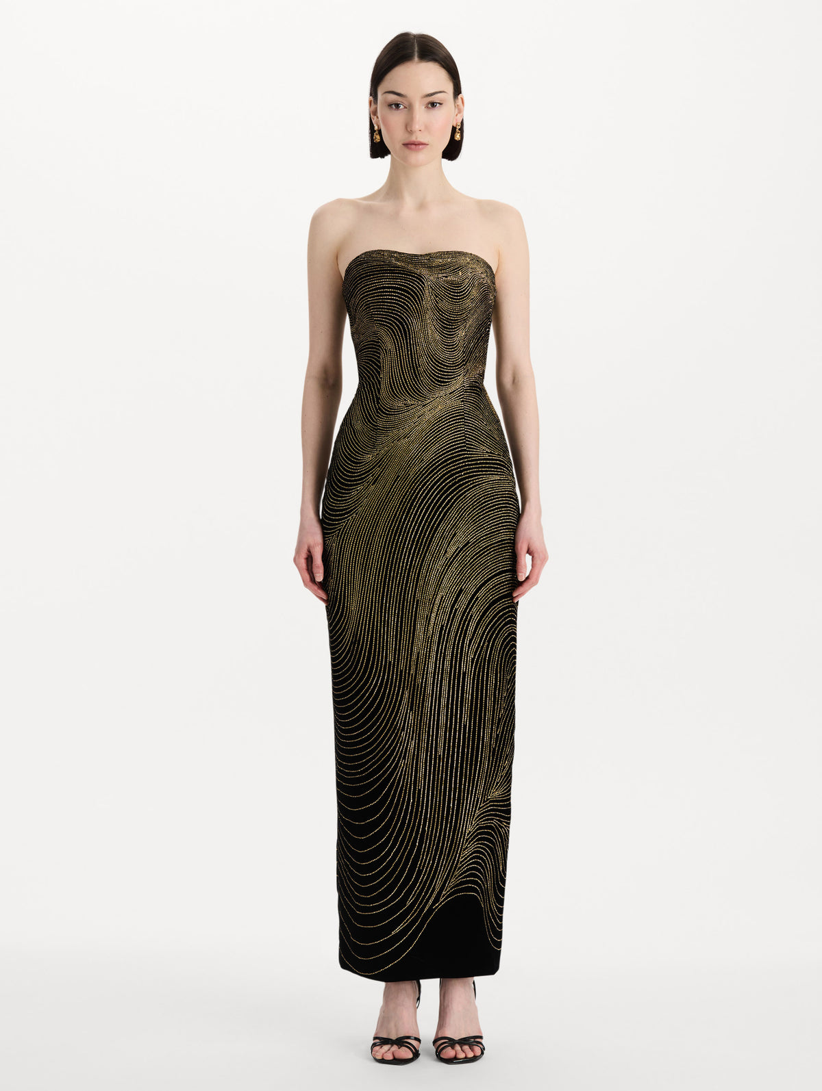 The model is wearing the beaded wave embroidered strapless cocktail dress in black and gold. Front view. 