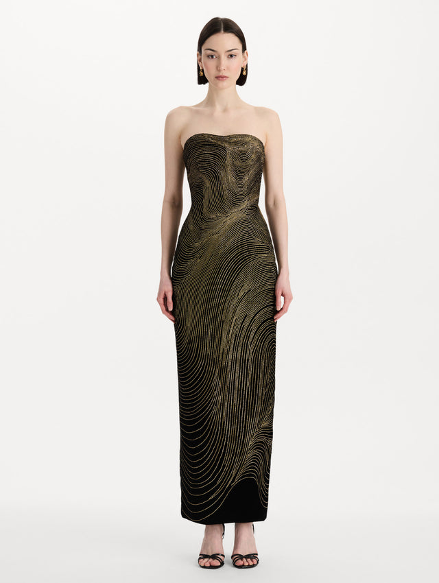 The model is wearing the beaded wave embroidered strapless cocktail dress in black and gold. Front view. 